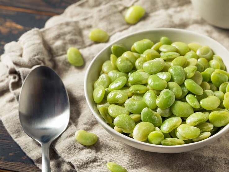 Weiße Schale mit Edamame-Bohnen und ein Löffel daneben. | © Getty Images/ bhofack2 via Canva.com