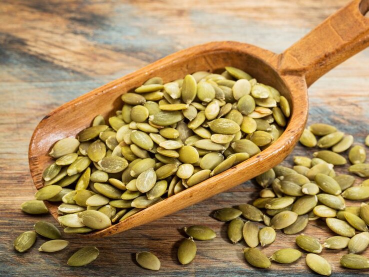 Holzschaufel mit grünen Kürbiskernen auf rustikalem Untergrund. | © Getty Images Pro/ marekuliasz via Canva.com