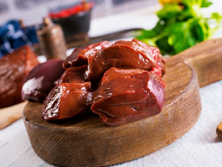 Roh geschnittene Leberstücke auf rundem Holzbrett in der Küche. | © Yana Gayvoronskaya via Canva.com 