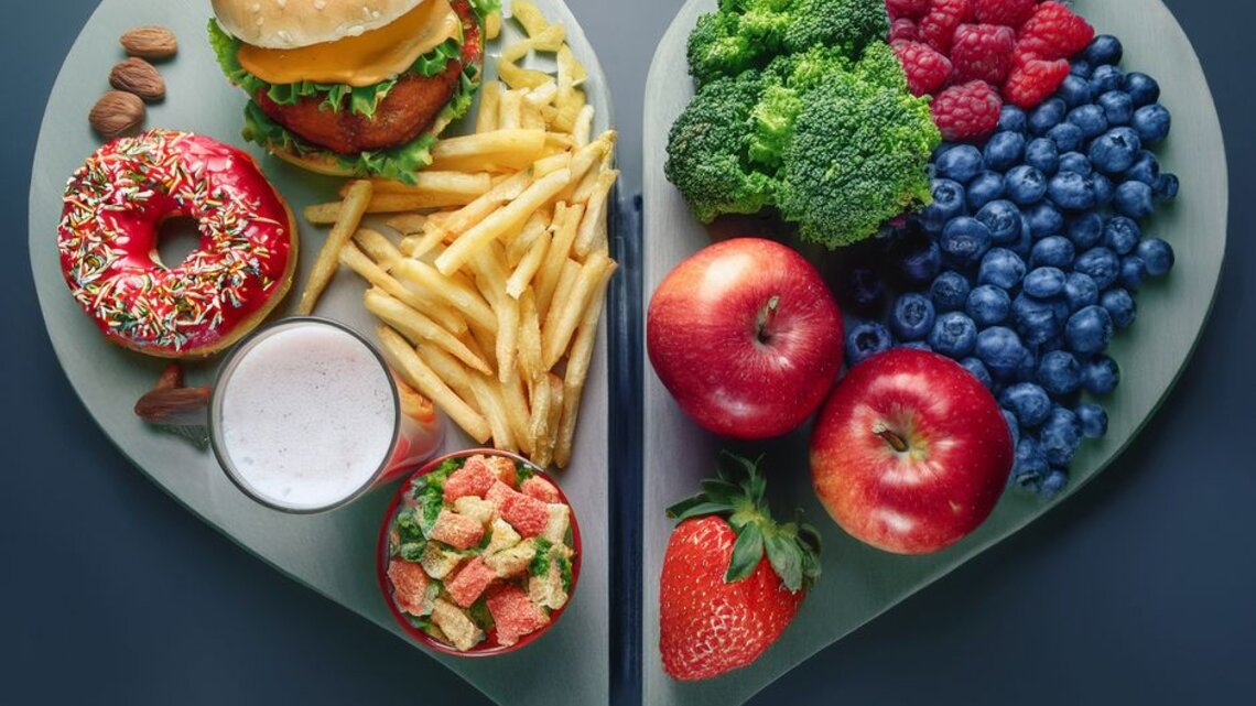 Herzförmige Platte, links mit Burger, Pommes, Donut, Süßigkeiten und Milchshake; rechts mit Brokkoli, Beeren, Äpfeln und Erdbeeren – klarer Kontrast zwischen stark verarbeiteten und frischen, nährstoffreichen Lebensmitteln.
