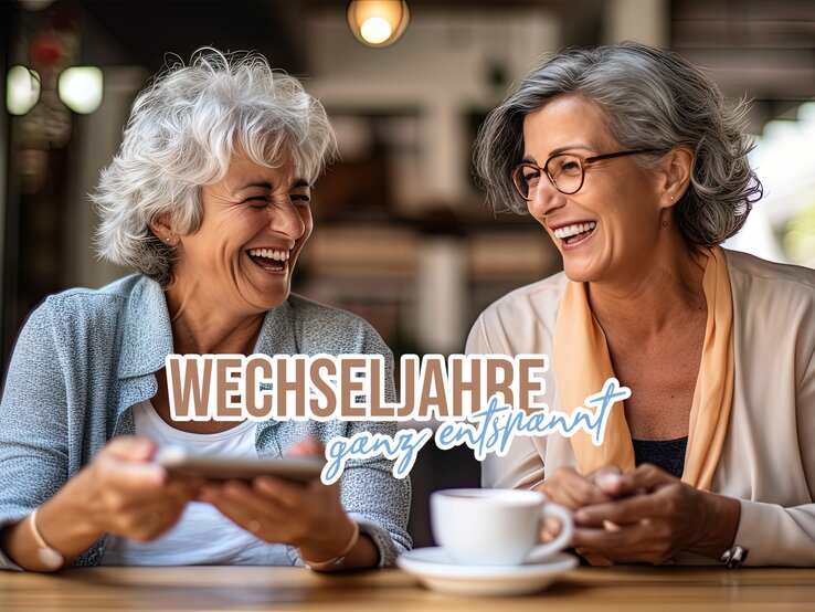 Hormon-Balance Titelbild Zwei Frauen im höheren Alter sitzen lachend zusammen in einem Café.