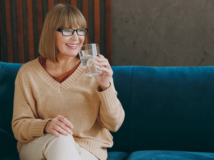 Dame mittleren Alters trinkt lächelnd ein Glas Wasser.