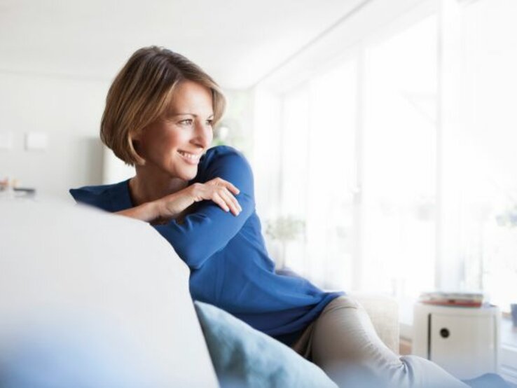 Frau mittleren Alters sitzt auf Sofa und schaut zur Seite