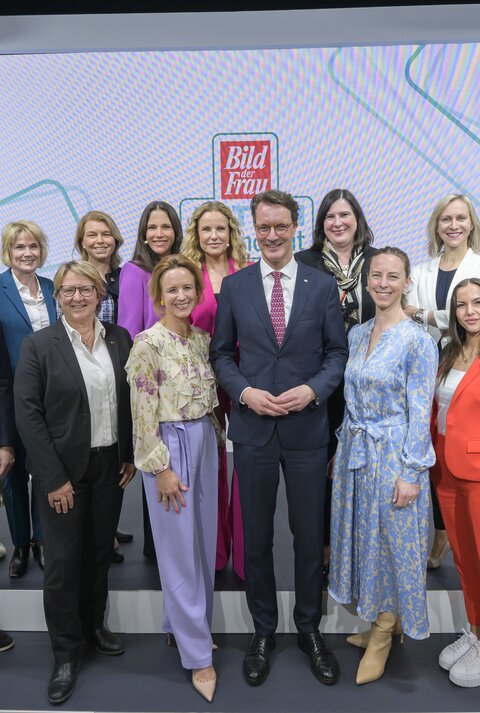 Vierzehn Frauen und zwei Männer in Businesskleidung posieren lächelnd auf einer Bühne vor „Bild der Frau“-Logos.