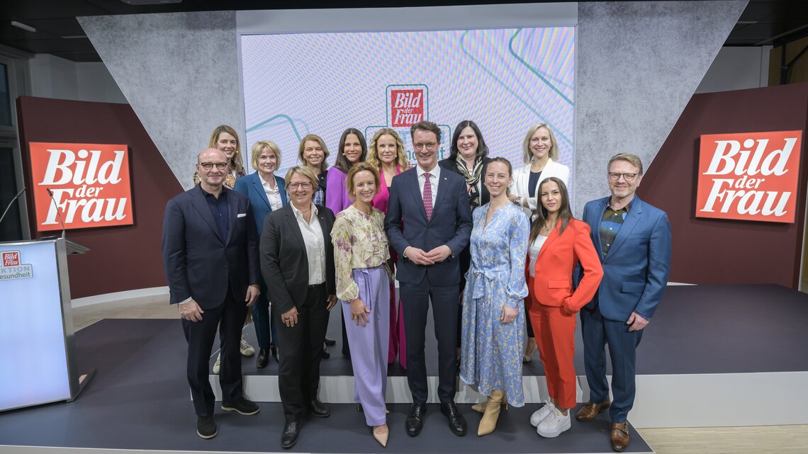 Vierzehn Frauen und zwei Männer in Businesskleidung posieren lächelnd auf einer Bühne vor „Bild der Frau“-Logos.