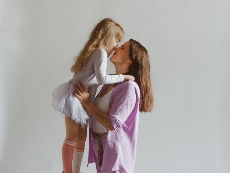 Junge Frau mit dunklen Haaren umarmt ihre kleine Tochter. 
