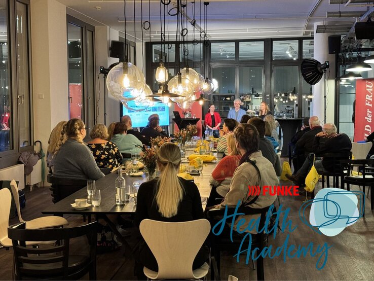 Sichere dir einen Platz bei unserem Event und erfahre mehr über Magnesium & Frauengesundheit. Gäste sitzen an langen, festlich gedeckten Tischen und lauschen einer Podiumsdiskussion mit drei Rednern in hellem Raum.