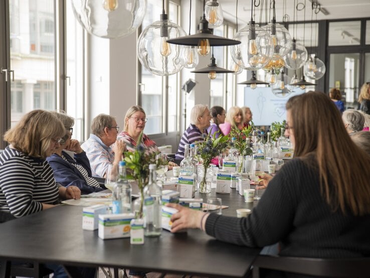 Gruppenrunde älterer Teilnehmerinnen in bunt gestreifter und gemusterter Kleidung bei einem Workshop an modern gedecktem Tisch. | © BILD der FRAU
