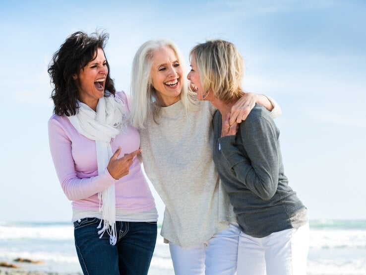 Porträt von drei Frauen am Strand, die lachen und Spaß haben.