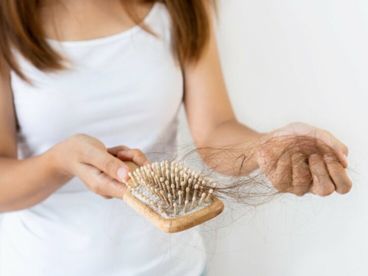 Frau hat Haarbürste in der Hand und entfernt die sich darin befindenen Haare | © Pattarisara – stock.adobe.com