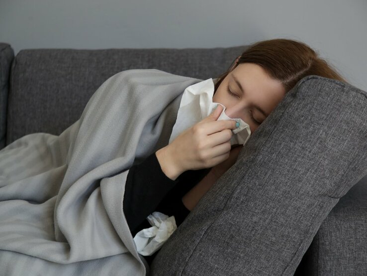 Frau liegt auf der Couch und schnäubt sich die Nase.