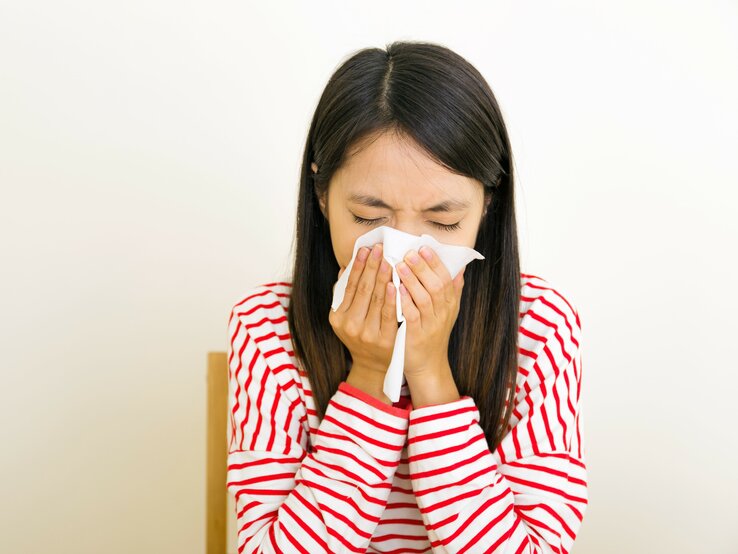 Eine dunkelhaarige Frau nießt in ein Taschentuch aufgrund von Allergie.