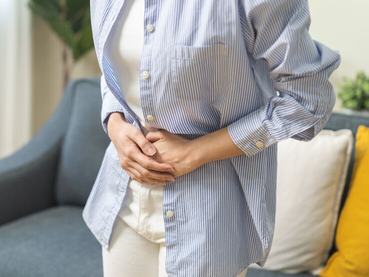 Junge Frau schaut zu ihrem aufgeblähtem Bauch und fasst diesen an.