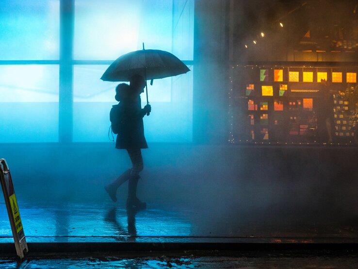 Neblig Innenstadt in Lower Manhattan eine Frau zu Fuß unter dem Regen im Dunkeln. | © gettyimages / LeoPatrizi