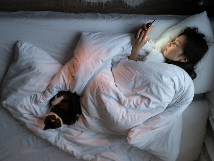 Frau liegt im Bett mit Handy in der Hand