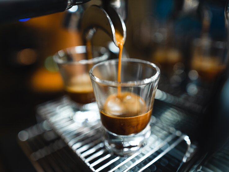 Frischer Espresso strömt geschmeidig aus einem Siebträger in ein transparentes Glas auf einem Metallgitter.