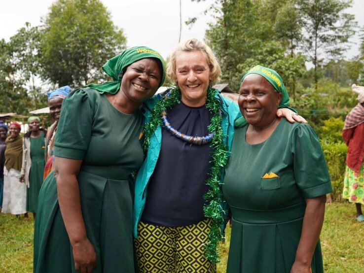 Preisträgerin Christina Schreiber Glückliche Szene: Drei Frauen umarmen sich im Grünen, lachen in die Kamera, im Hintergrund weitere Frauen in traditioneller Kleidung.