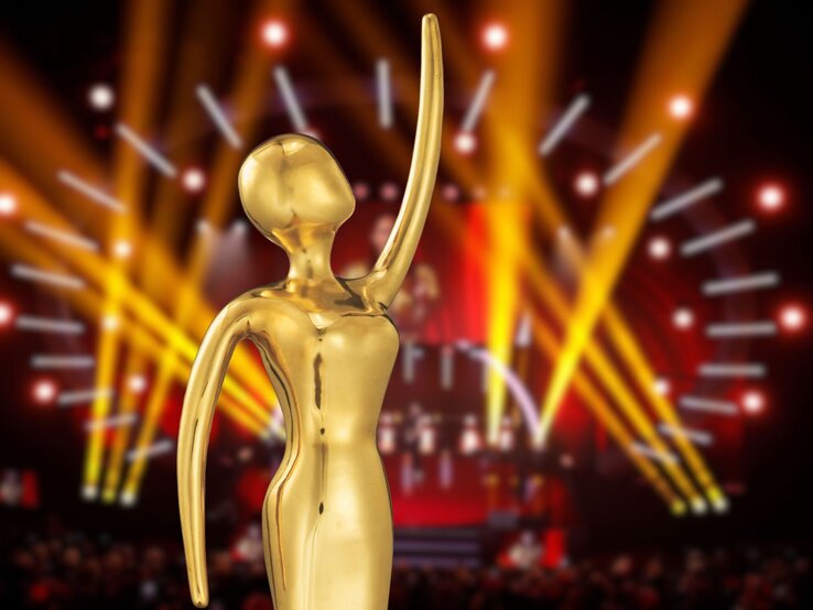 Promis unterstützen GOLDENE BILD der FRAU Glänzende Preisfigur in abstrakter Form steht vor strahlenden Lichtstrahlen auf festlich beleuchteter Showbühne.