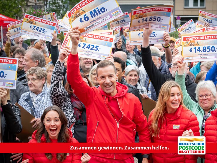 Postcode Lotterie: Zusammen gewinnen, zusammen helfen Gruppe von Gewinnern der Deutschen Postcode Lotterie hält lachend ihre Gewinnschecks in die Höhe.