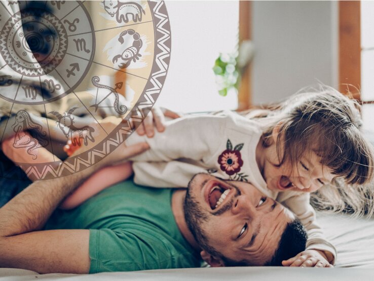 Ein fröhlicher Vater liegt auf dem Rücken und spielt mit seiner lachenden kleinen Tochter, die auf ihm liegt. Über ihnen schwebt eine transparente Scheibe mit verschiedenen astrologischen Symbolen. Sie befinden sich in einem hell erleuchteten Raum, was eine warme und liebevolle Atmosphäre schafft.