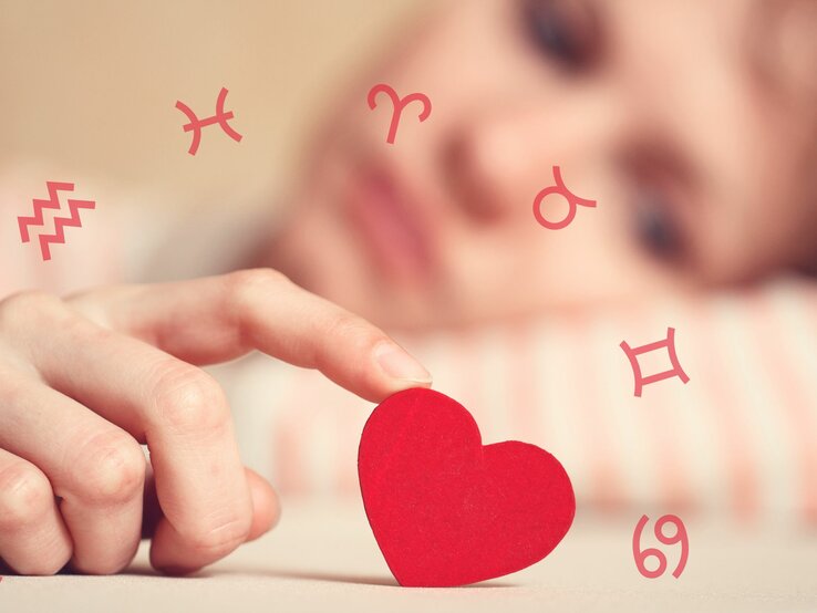 Die Hand einer Frau wiegt ein rotes Herz, umgeben von den Symbolen der Tierkreiszeichen.