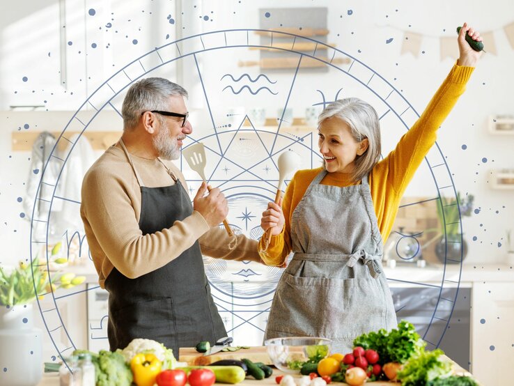 Ein Paar tanzt und hat Spaß in der Küche und nutzt Kochlöffel als Mikrofone. Im Hintergrund ist der Tierkreis mit den astrologischen Symbolen der Sternzeichen zu sehen. 