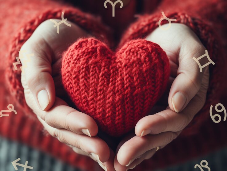 Frauenhände halten ein gestricktes rotes Herz. Darum herum ist der Tierkreis zu sehen mit den astrologischen Symbolen der Sternzeichen. 