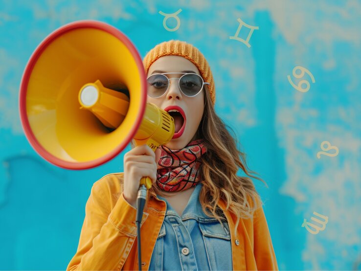 Eine Junge Frau mit orange-farbener Mütze steht mit einem Megafon vor dem Mund.