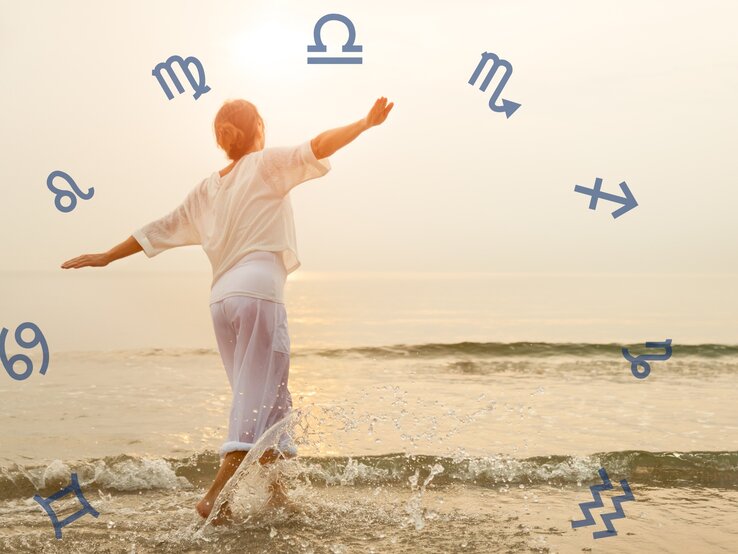 Das Bild zeigt eine Person, die an einem Strand steht und ins Wasser tritt. Sie trägt lockere weiße Kleidung und breitet die Arme aus, als würde sie die Freiheit und die Natur genießen. Um die Person herum sind verschiedene astrologische Symbole in einem Kreis angeordnet. Die Szene ist in warmes, weiches Licht getaucht, was eine friedliche und harmonische Atmosphäre erzeugt.