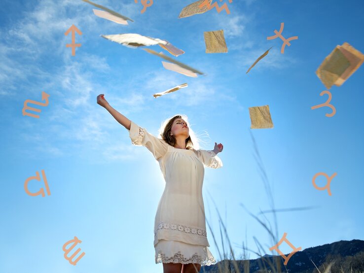 Eine Frau in einem weißen Kleid steht in einer weiten Landschaft unter einem klaren blauen Himmel. Sie hebt ihre Arme in die Luft, während um sie herum Papierblätter und Symbole der Sternzeichen schweben. Die Szene vermittelt ein Gefühl von Freiheit, Leichtigkeit und spiritueller Verbindung.
