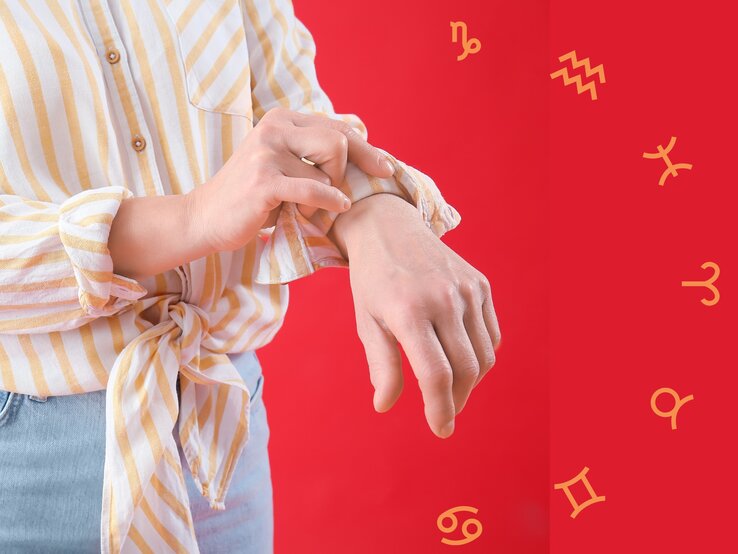Eine Person in einer gestreiften Bluse krempelt ihren Ärmel hoch, während sie sich die Handgelenke betrachtet. Im Hintergrund sind auf einem roten Untergrund astrologische Symbole der Tierkreiszeichen zu sehen. Die Szene symbolisiert Selbstreflexion und das Durchstehen von Herausforderungen.