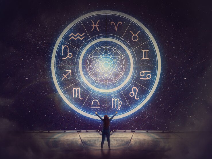 Eine Person steht vor einem großen, leuchtenden astrologischen Rad, das alle zwölf Tierkreiszeichen zeigt. Der Nachthimmel im Hintergrund ist voller funkelnder Sterne, und die Szene vermittelt eine mystische und kosmische Atmosphäre.