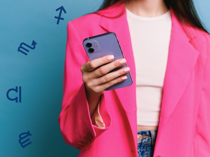 Eine Frau in einem auffälligen pinken Blazer hält ein Smartphone in der Hand. Der Hintergrund ist in einem lebendigen Blau gehalten, und astrologische Symbole schweben dezent um die Szene herum. Die Frau trägt ein schlichtes weißes Top und Jeans, ihre gepflegten Nägel sind in einem natürlichen Ton lackiert. Das Bild vermittelt einen modernen und energiegeladenen Stil mit einem Hauch von Astrologie.