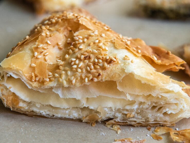 Tiropita Ein Stück Tiropita auf einem Blech mit Backpapier. Alles nah und von vorne fotografiert.