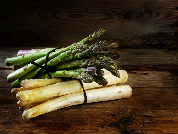 gebundener weißer und grüner Spargel auf Holzuntergrund.