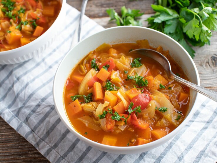 Weiße Schüssel voll Kohlsuppe mit Karotten und Paprika. 