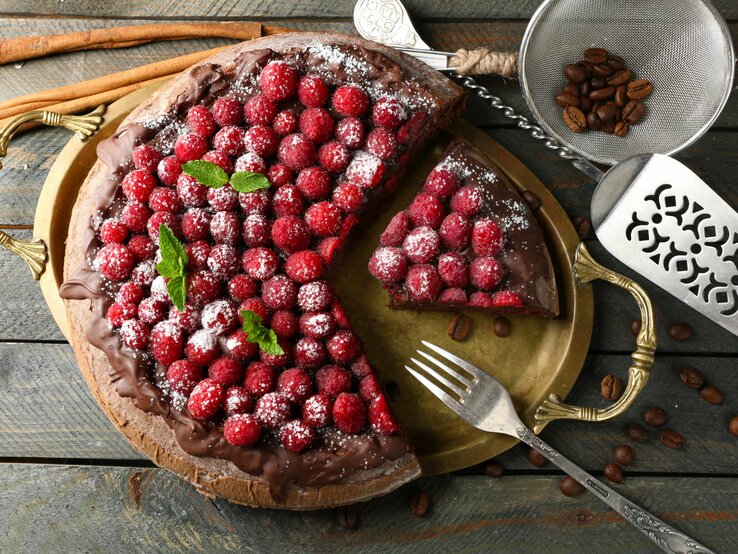 Himbeer-Schokokuchen mit Puderzucker bestreut auf rustikalem Holztisch, neben Kaffeebohnen.