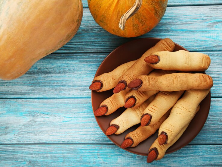 Halloween-Kekse-Gruselfinger Ein brauner Teller mit den Keksen auf einem blauen Holztisch mit Kürbissen am oberen Bildrand. Alles direkt von oben fotografiert.