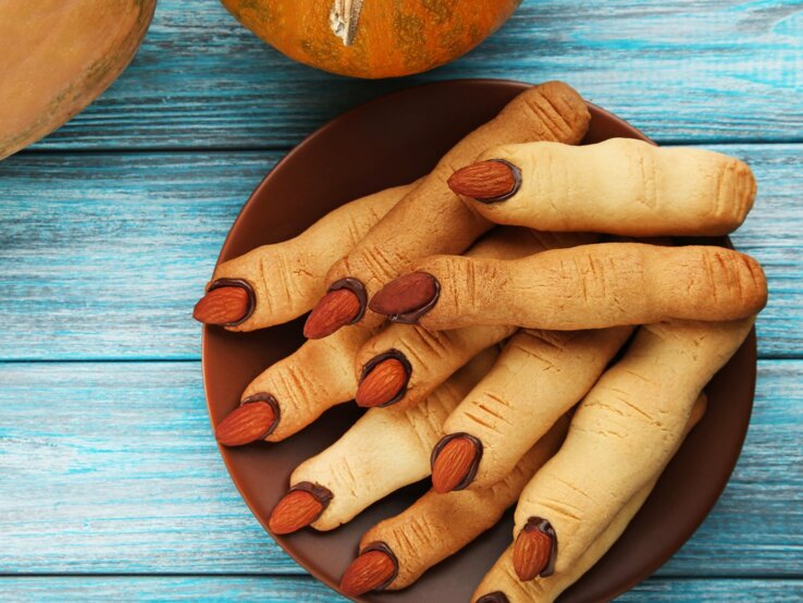 Halloween-Kekse-Gruselfinger Ein brauner Teller mit den Keksen auf einem blauen Holztisch mit Kürbissen am oberen Bildrand. Alles direkt von oben fotografiert.