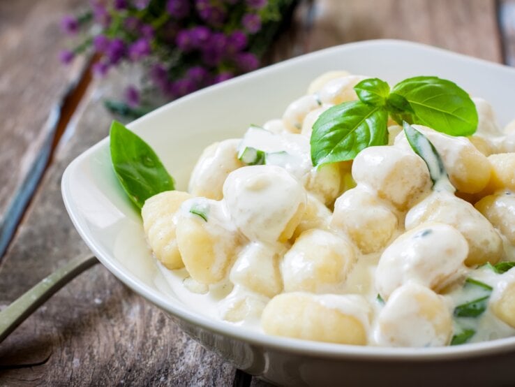 Ein weißer Teller befüllt mit Low-Carb-Gnocchi in cremiger Soße auf Holztisch.