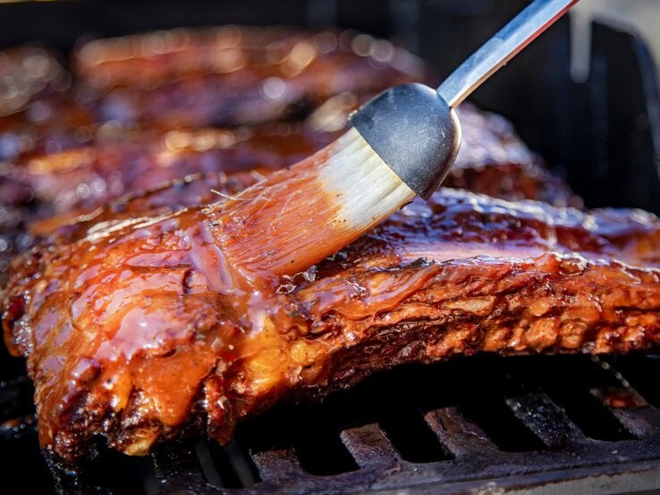 Spareribs-Grill Die Spareribs von der Seite auf dem Grill fotografiert, während sie gerade mit Marinad eeingepinselt werden.