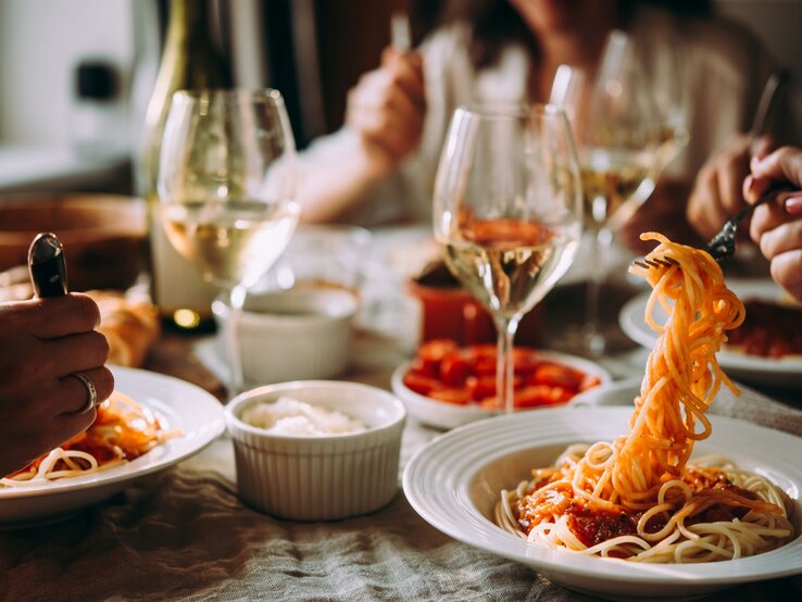 An einem Tisch wird Pasta gegessen und wein getrunken. Gesichter sind nicht zu sehen.  | © AdobeStock/FornStudio