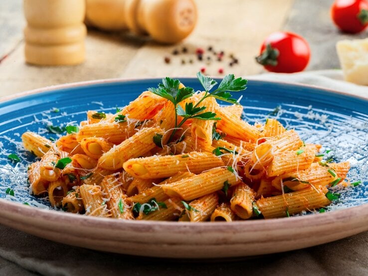 Penne arrabiata Penne in leuchtender Tomatensauce mit Parmesan und Kräutern serviert auf einem blauen Teller vor rustikalem Hintergrund.
