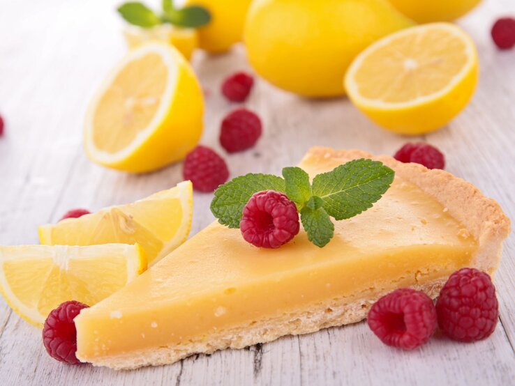 Zitronenkuchen Low Carb Zitronenkuchen-Stück im Vordergrund, belegt mit Himbeeren und im Hintergrund aufgeschnittene Zitronen