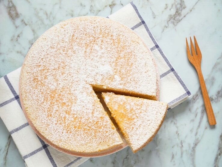 Ein Low Carb Joghurtkuchen von oben fotografiert, ein Stück ist angeschnitten und eine Gabel liegt recht davon auf dem Tisch.