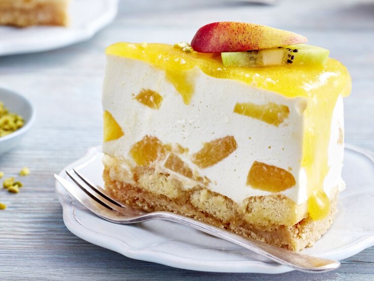 Tropische-Tiramisu-Torte Ein Tortenstück auf einem weißen Teller von der Seite auf einem hellen Tisch fotografiert.