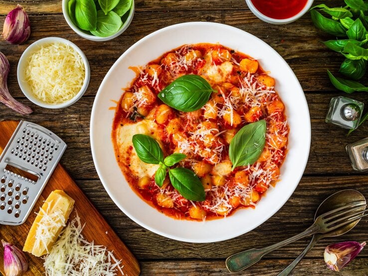 Frisch zubereitete Gnocchi in Tomatensauce mit Basilikumblättern und geriebenem Parmesan auf rustikalem Holztisch.