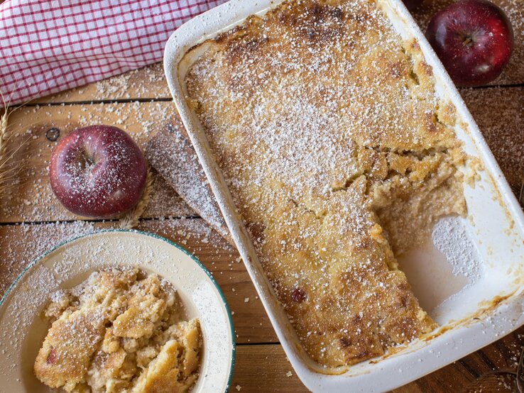 Apfel Quark Auflauf Rezept Frisch gebackener Apfelauflauf mit goldbrauner Kruste und Puderzucker in Auflaufform auf rustikalem Holztisch.