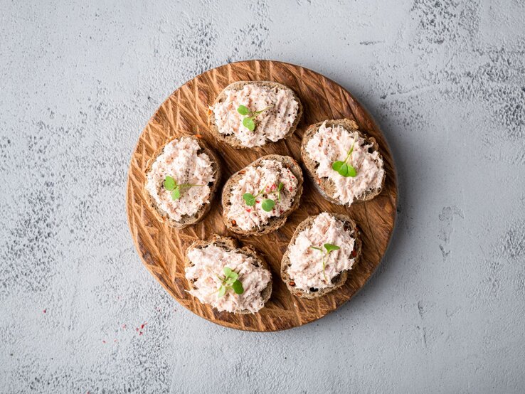Draufsicht auf  ein Holzbrett, darauf mehrere Scheiben Thunfisch-Bruschetta.