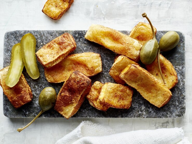 Airfryer-Brie-Chips Die knusprigen Käsechips auf einem rechteckigen Teller und grauem Untergrund. Alles direkt von oben fotografiert.